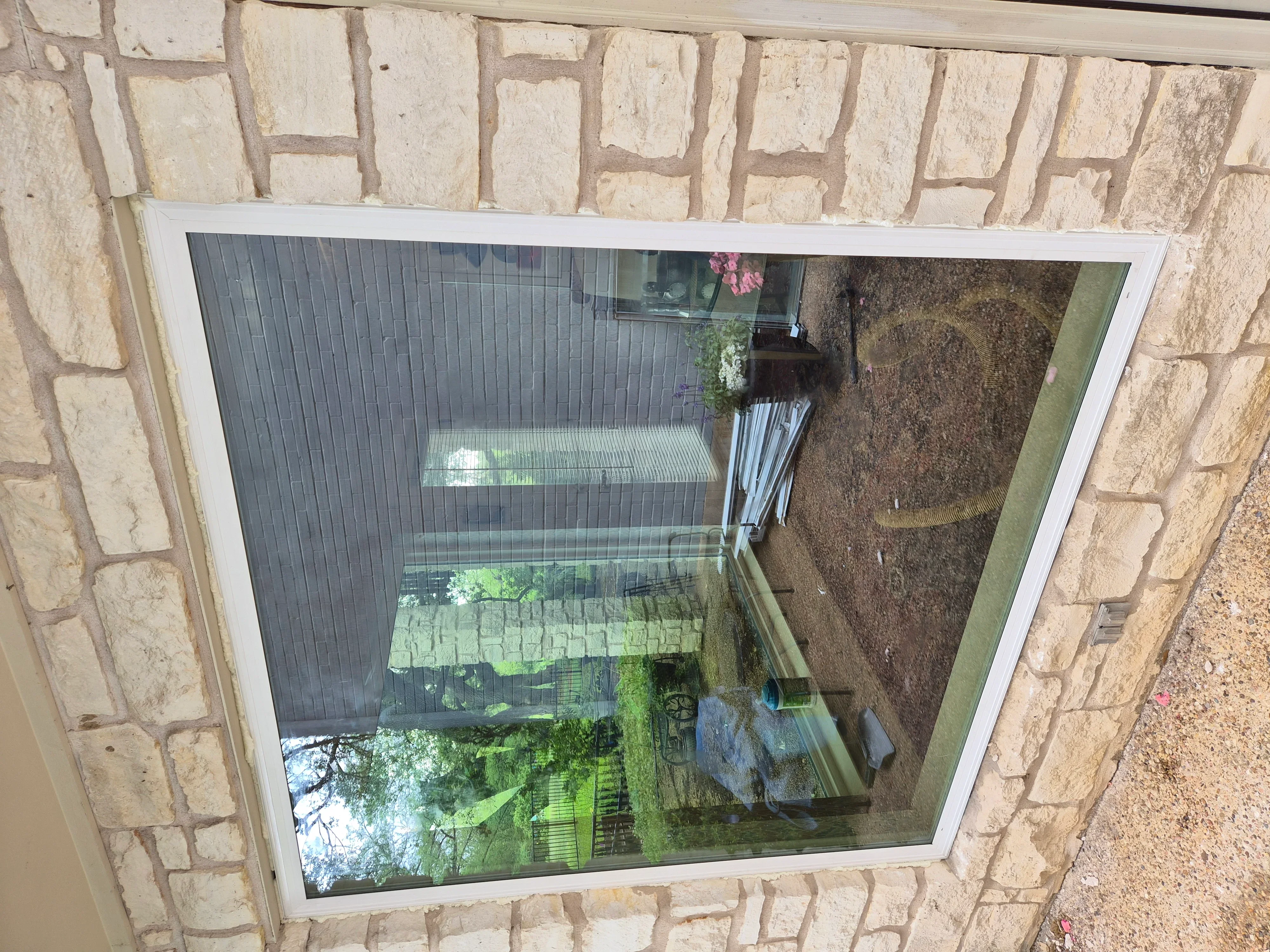 White-framed window installed in tan stone exterior wall overlooking backyard