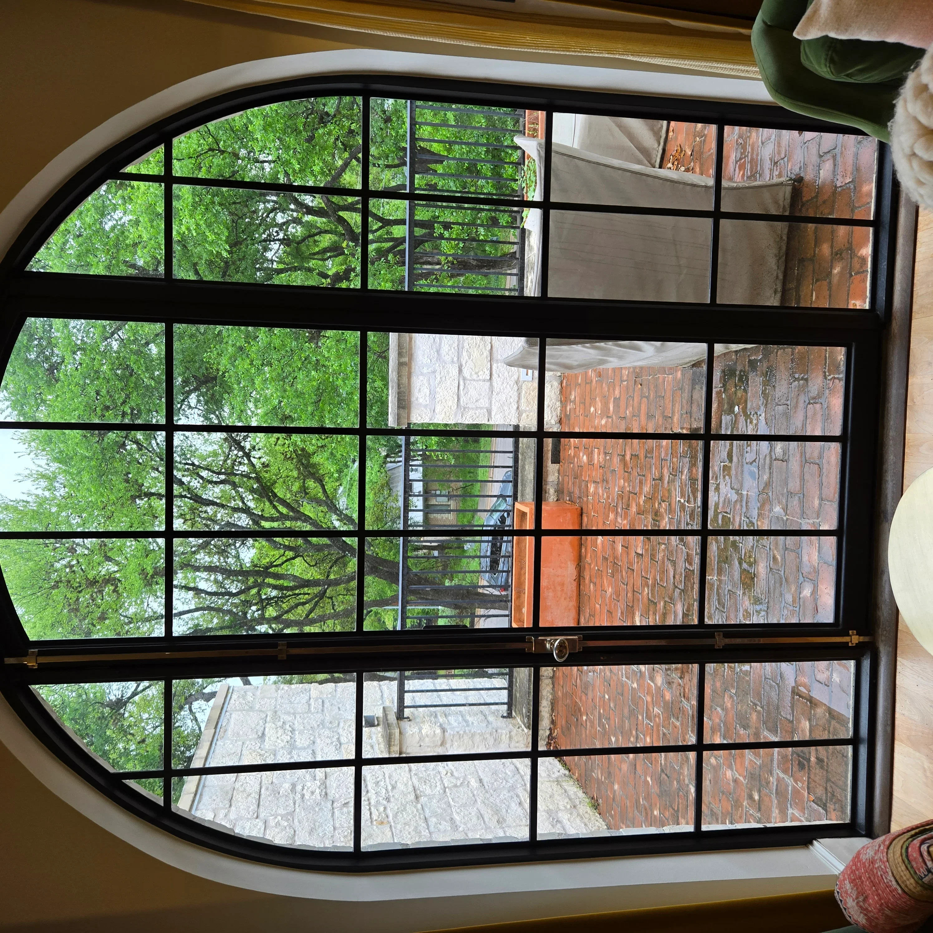 Black-framed arched window with 20 panes overlooking green trees and brick buildings