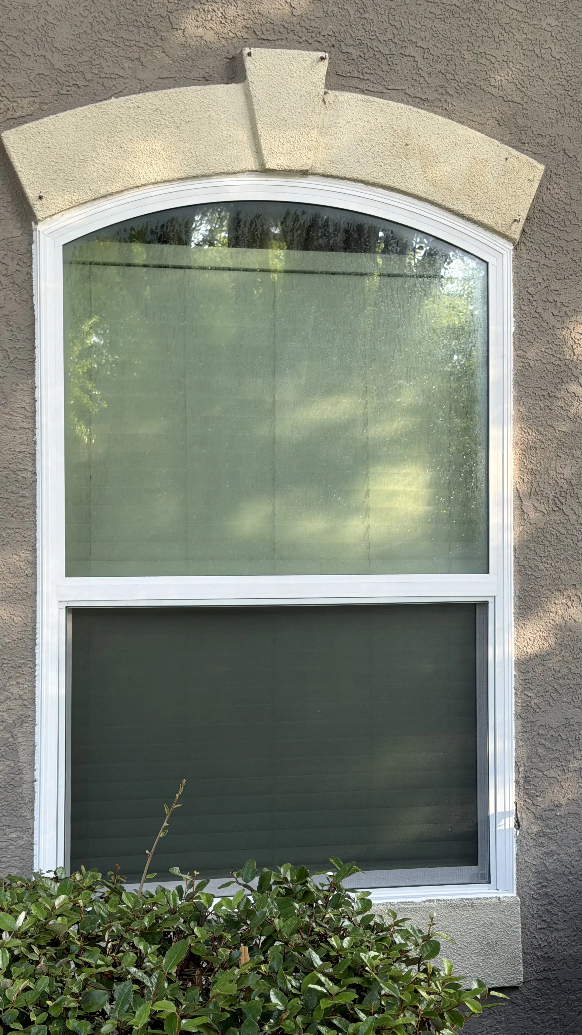 White arched window with upper curved glass pane installed in stucco exterior wall