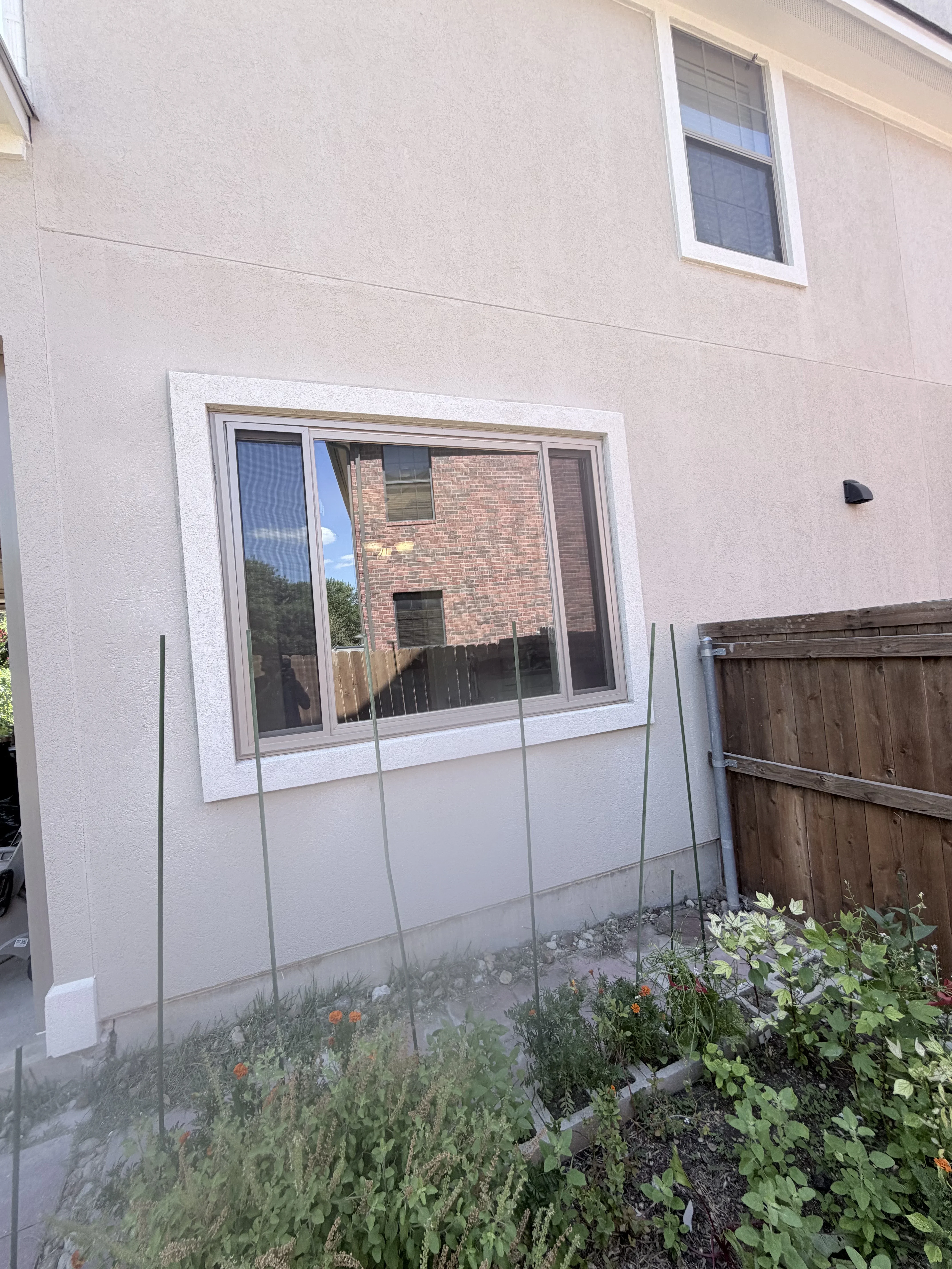 White-framed sliding glass door installed on tan stucco wall with garden below