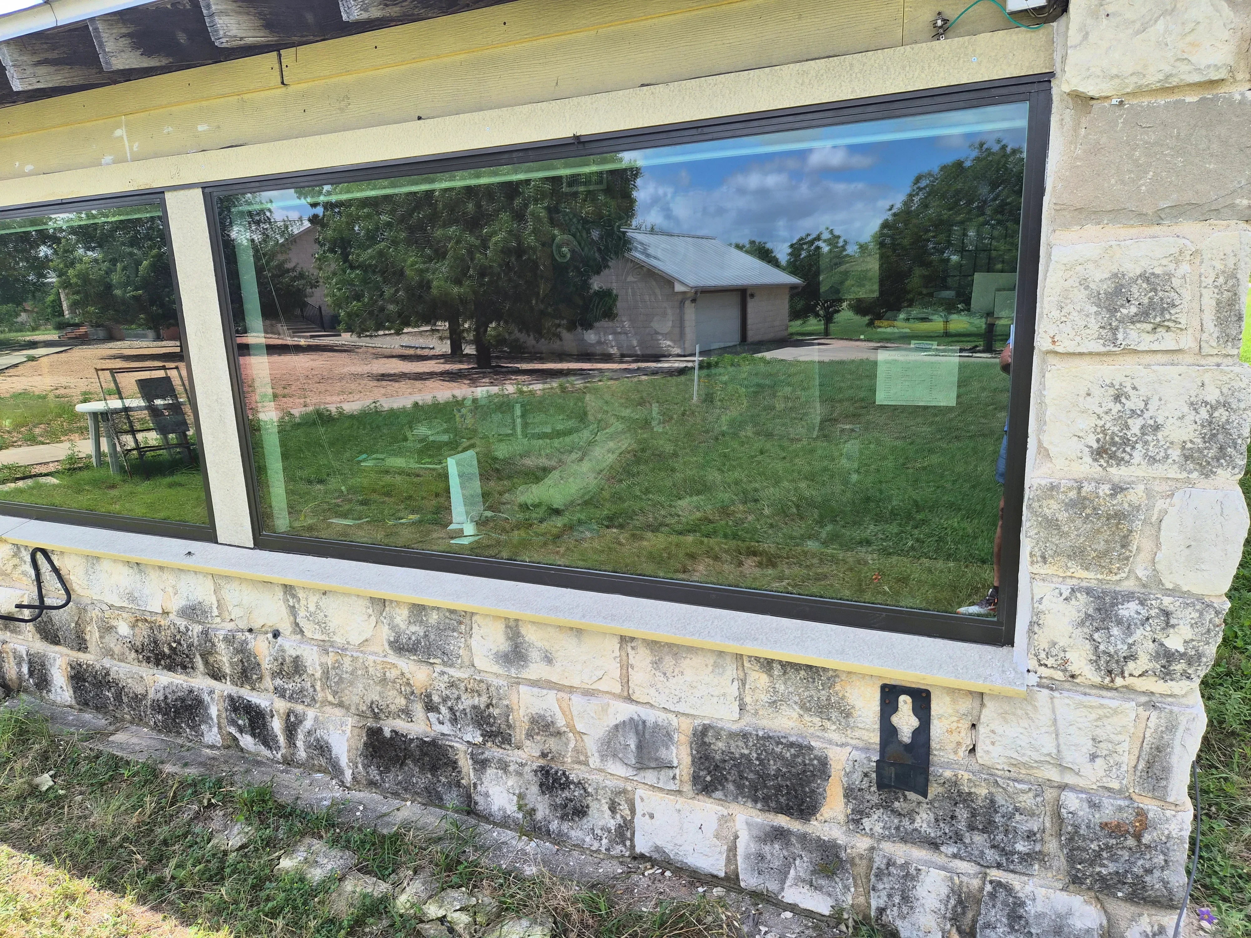 Large picture window with dark frame installed in stone exterior wall overlooking rural property