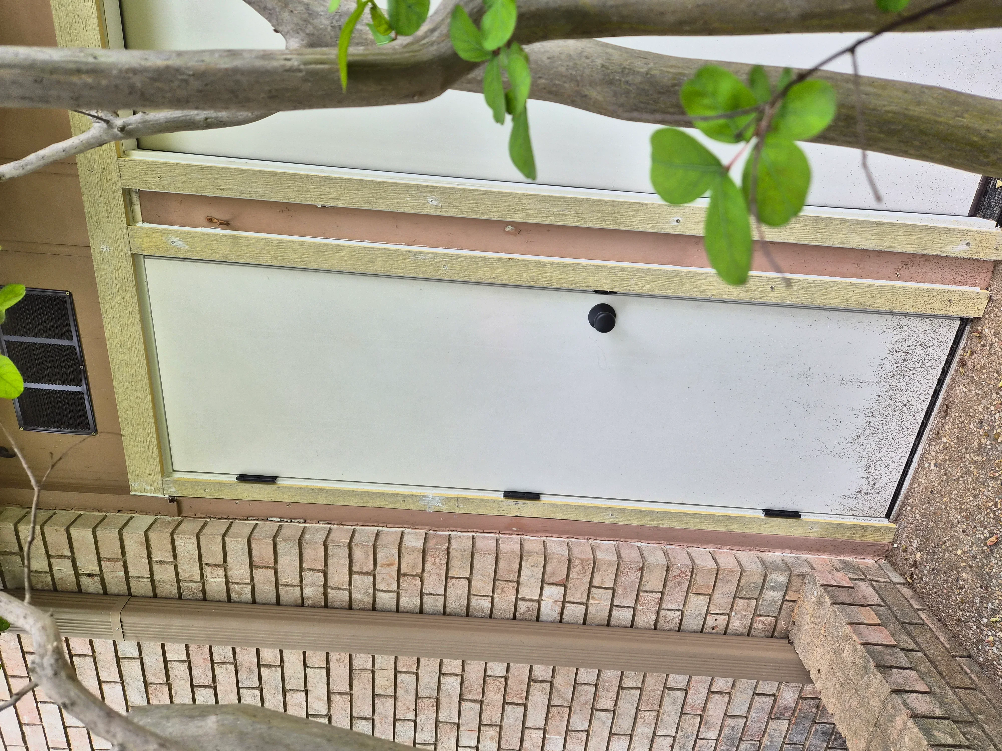 Wood-framed basement window well with clear polycarbonate cover installed against brick foundation