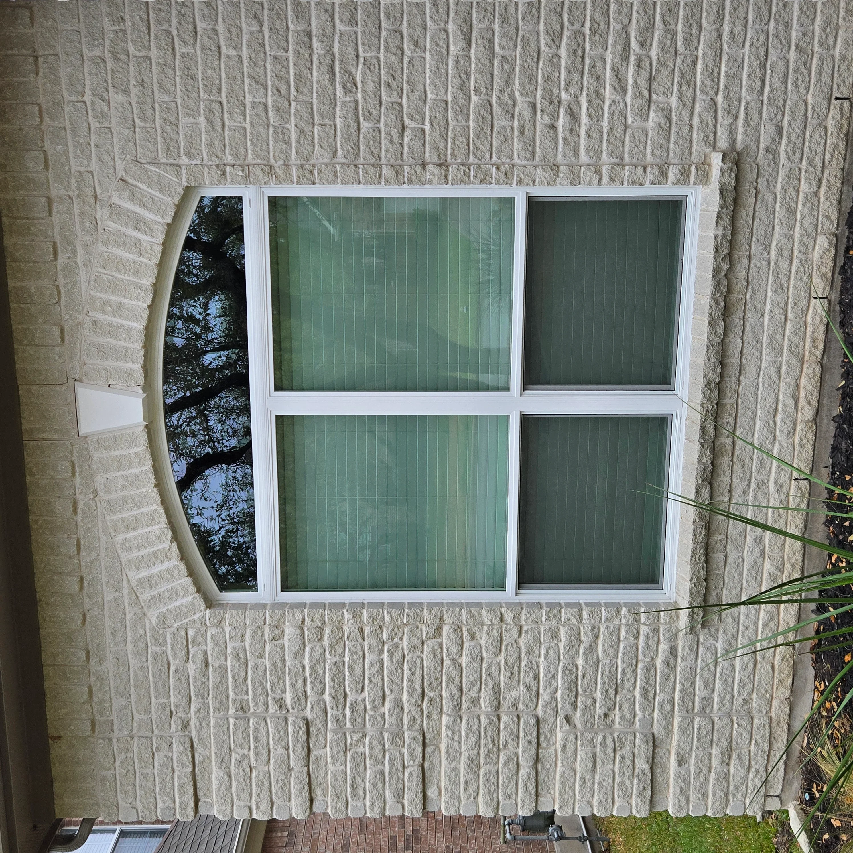 White vinyl four-pane window installed in light brick exterior wall with vertical blinds