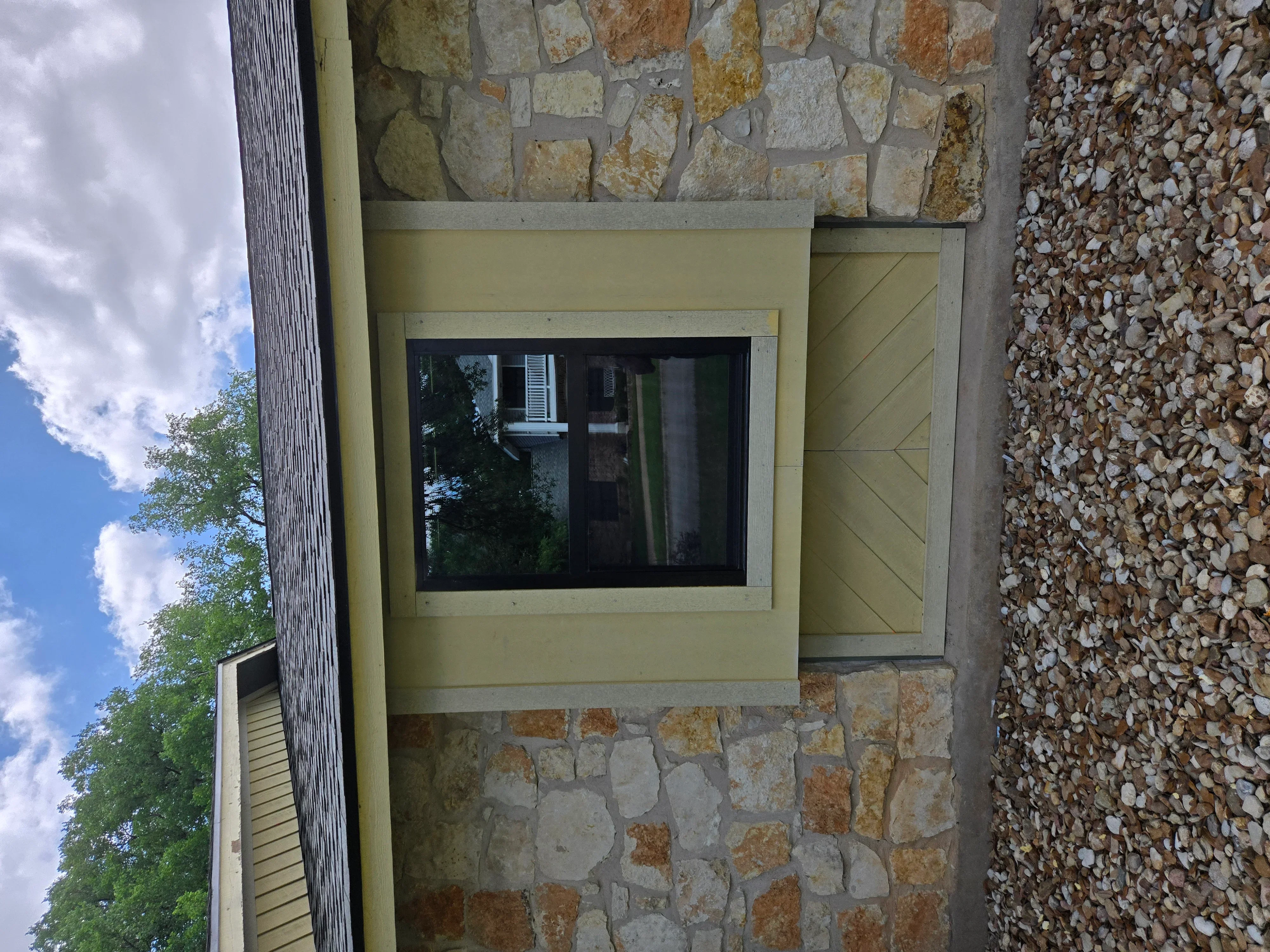 Large black-framed window installed in cream stucco wall with stone veneer cladding