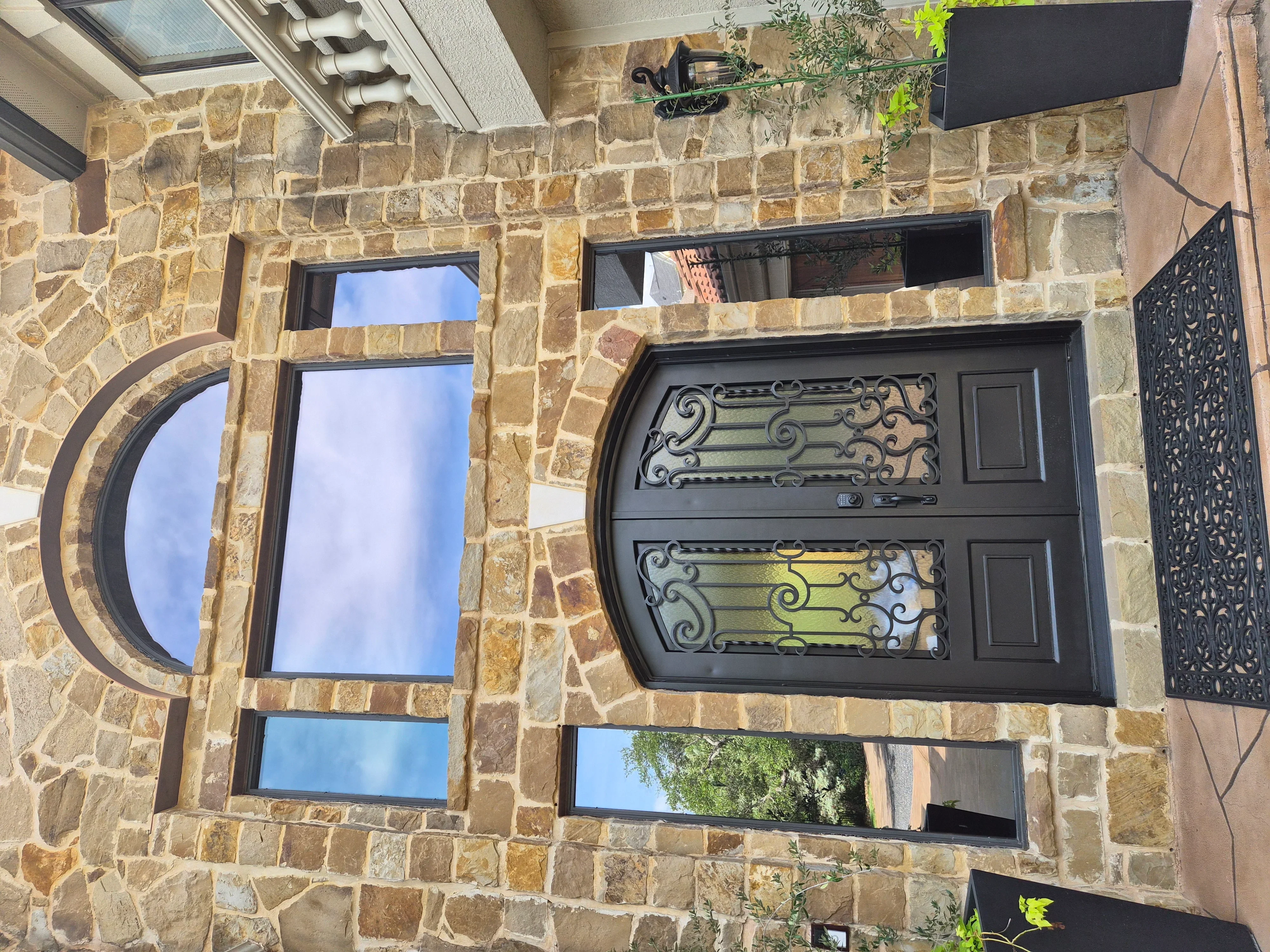 Black ornamental entry door with decorative glass and matching black-framed windows on stone exterior