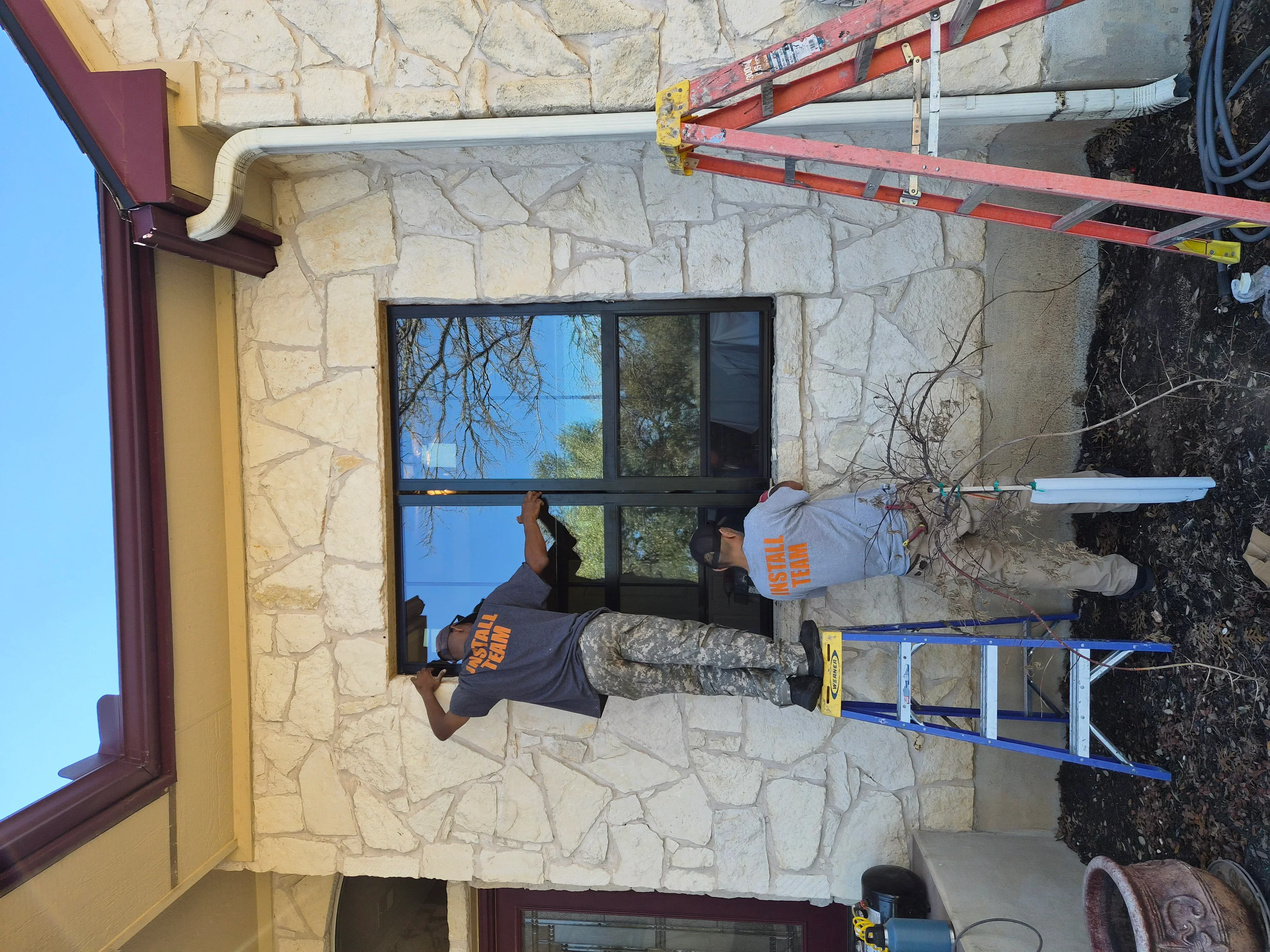 Two installers fitting black-framed window into stone wall facade during installation