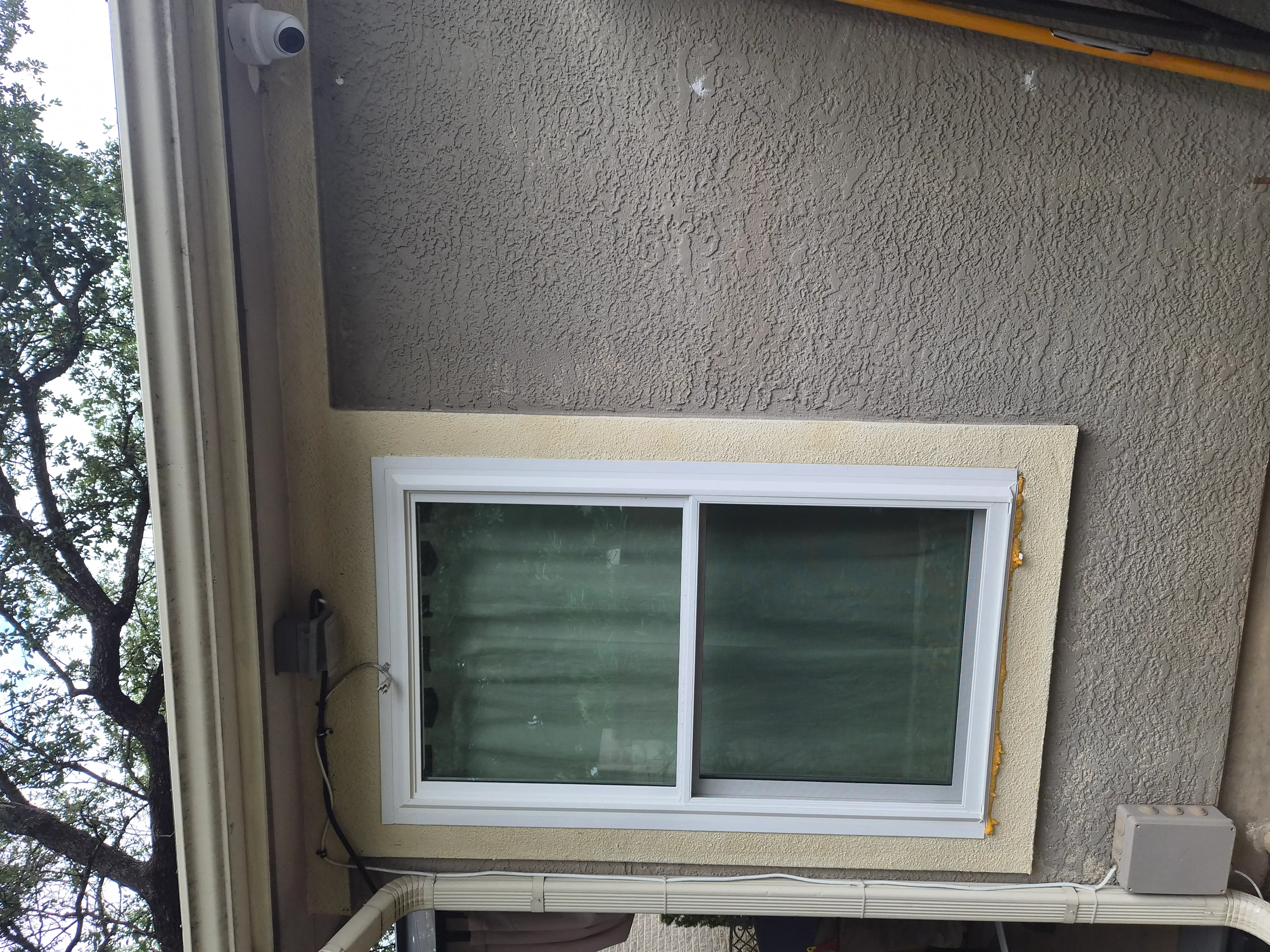 White vinyl sliding window installed in stucco exterior wall with green-tinted glass panes
