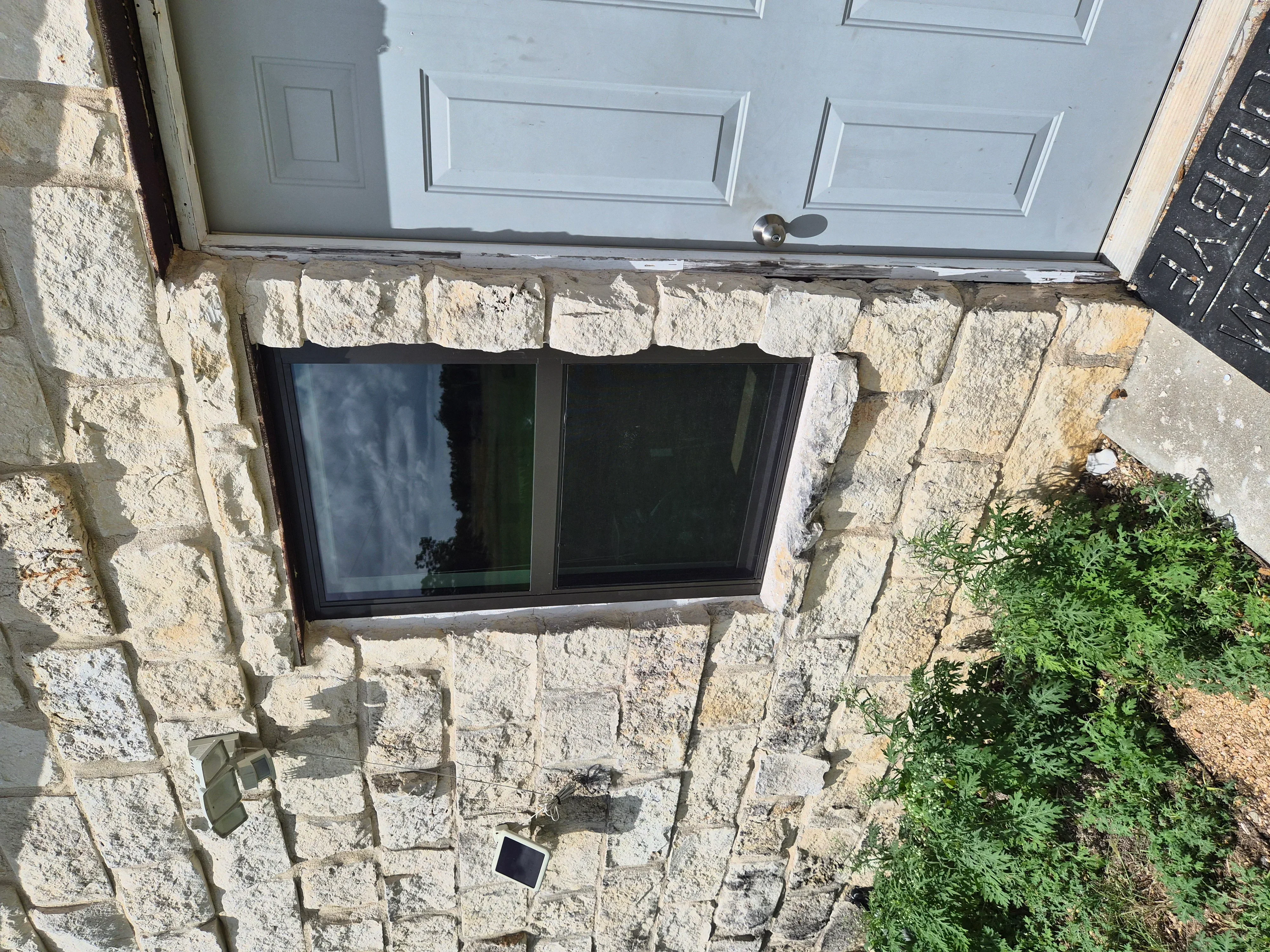 Black-framed basement window installed in cream-colored stone foundation wall