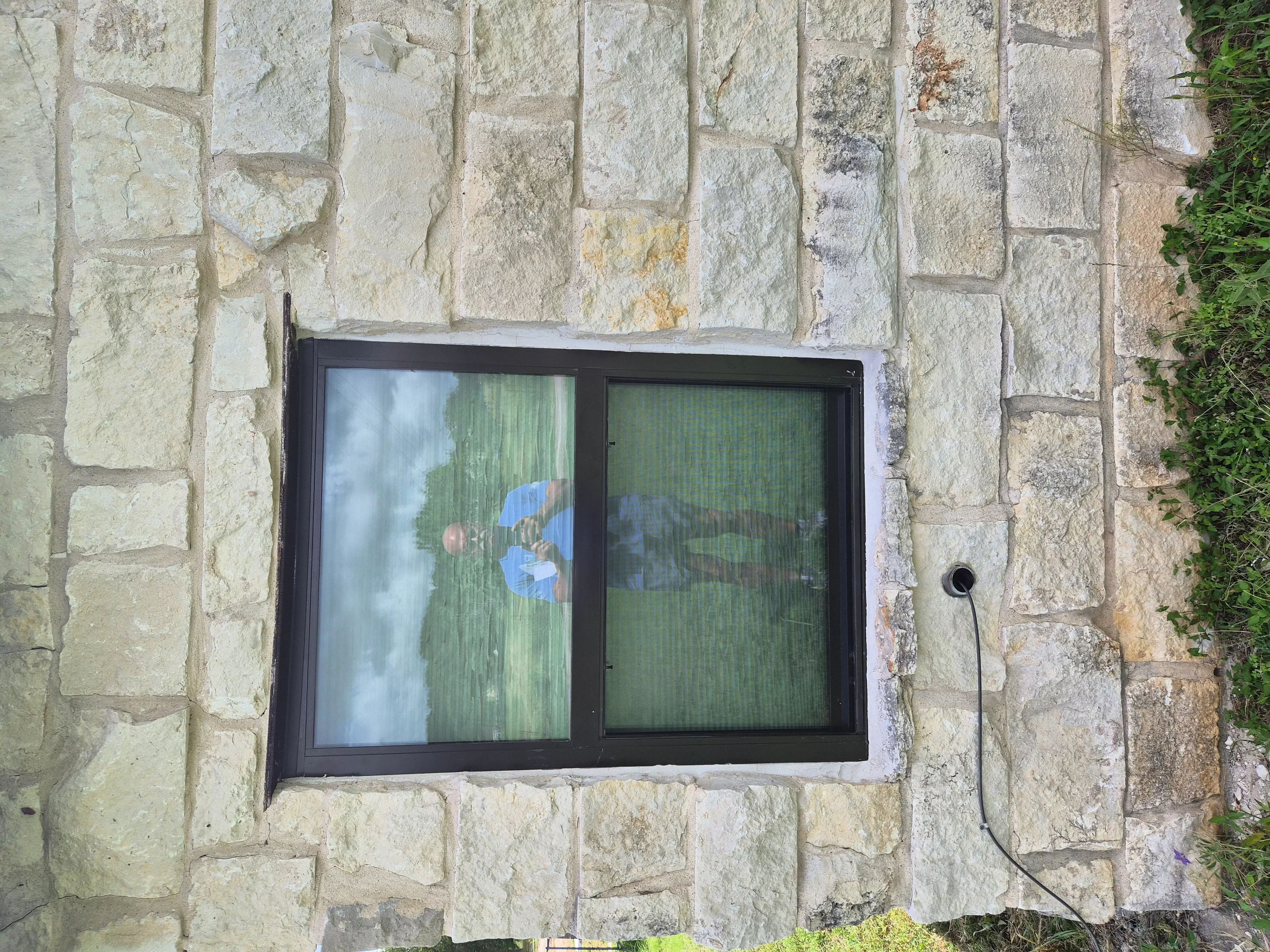 Black sliding window installed in cream and tan stone wall with ivy growth on right edge