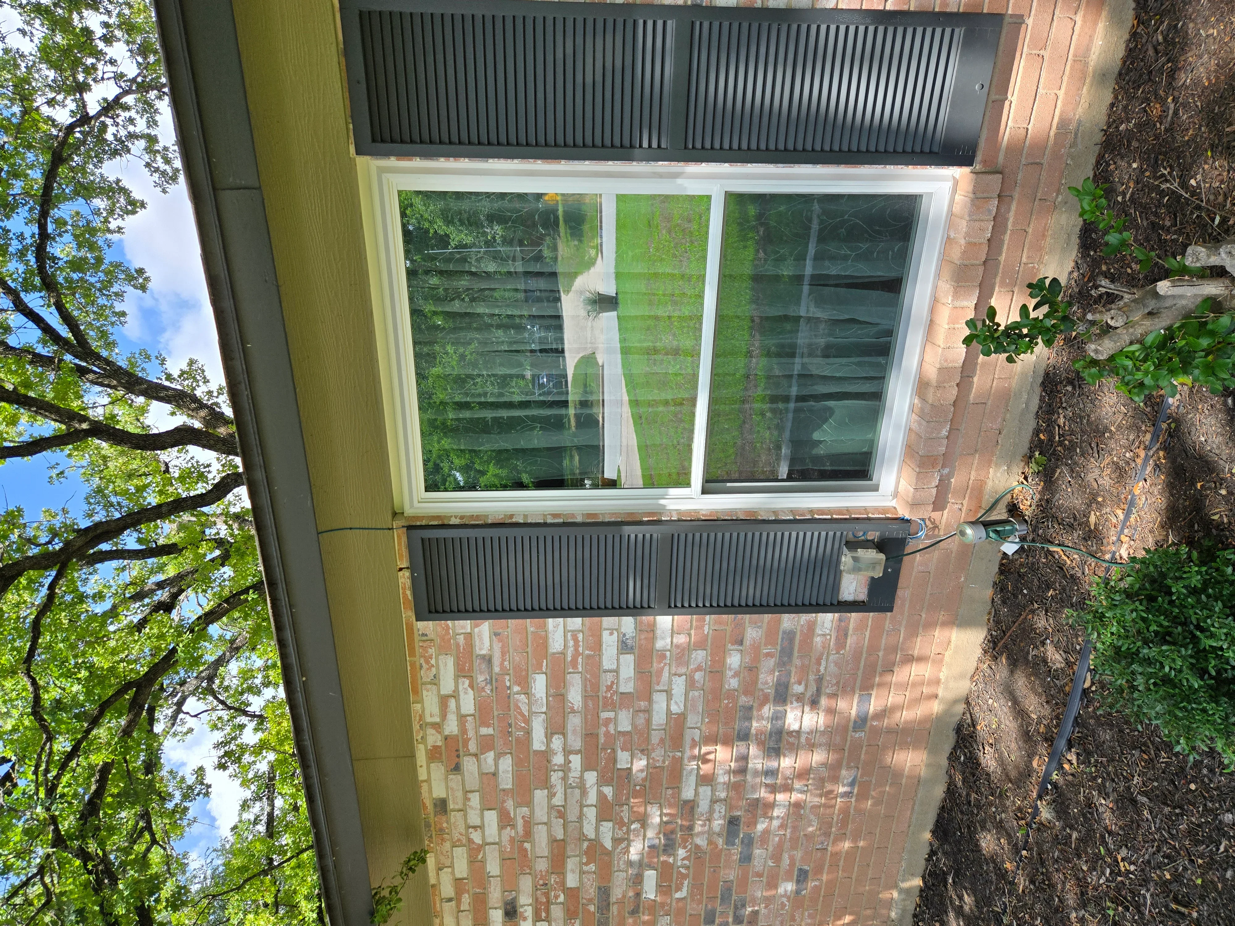 Triple-pane white sliding window with dark shutters installed on brick home exterior