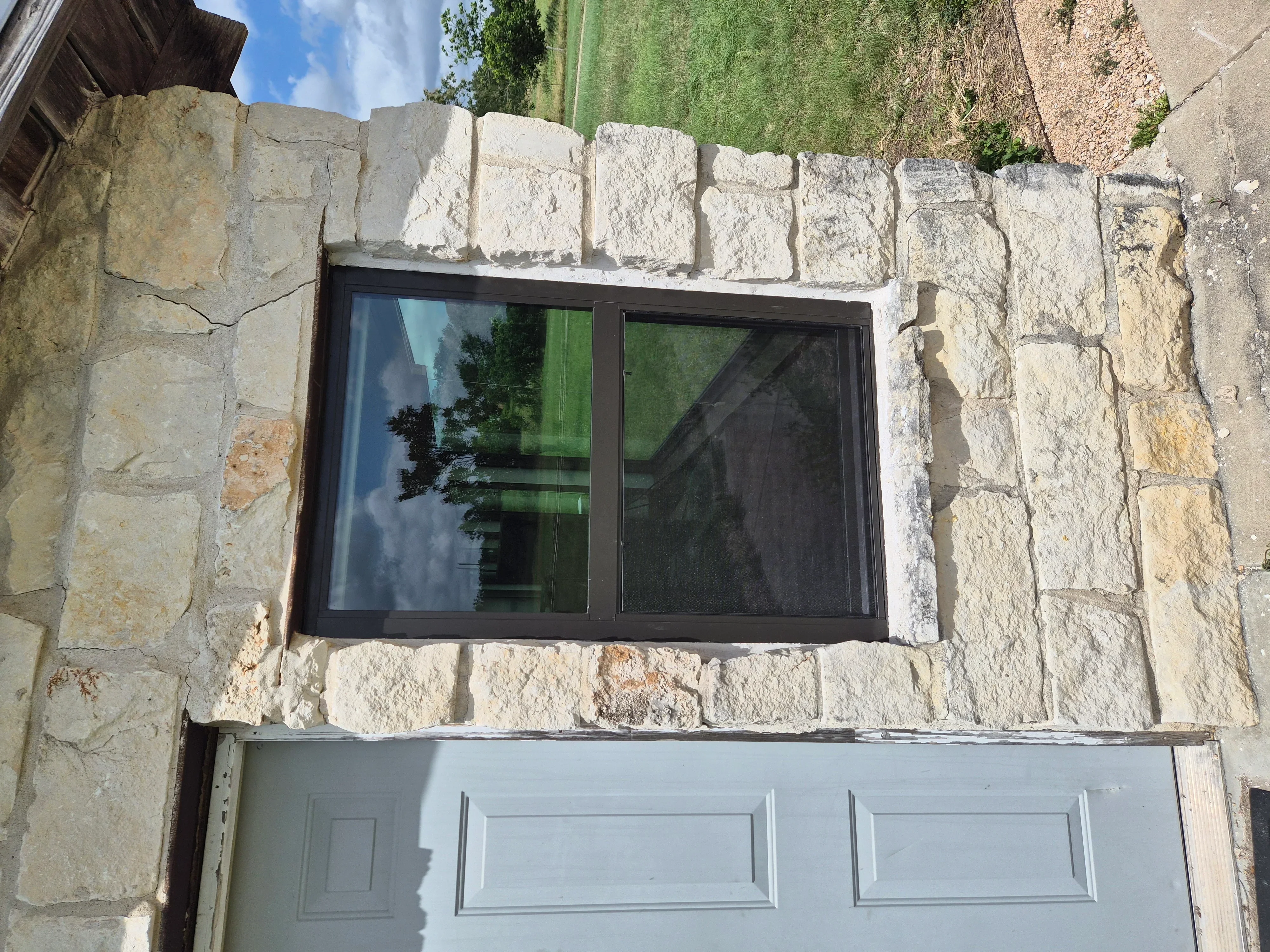Black-framed sliding window installed in limestone stone wall facade